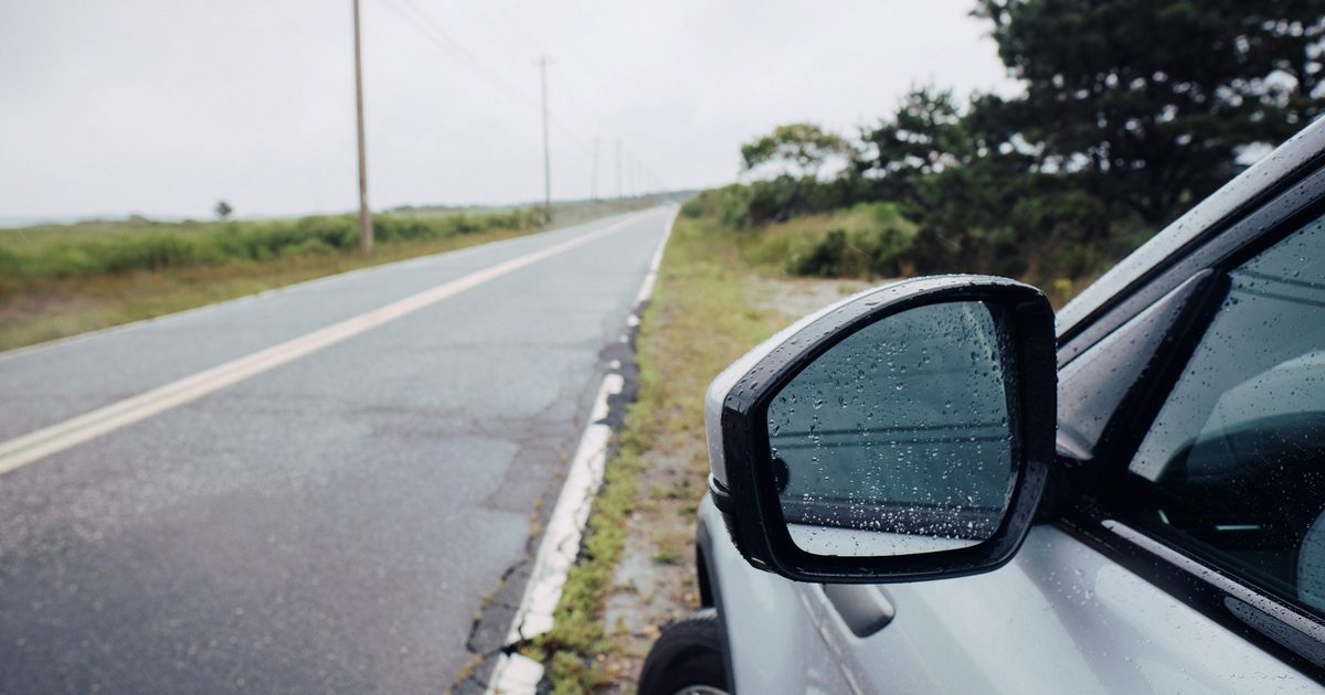 雨つぶのついた白い車のドアミラーと、まっすぐな道路